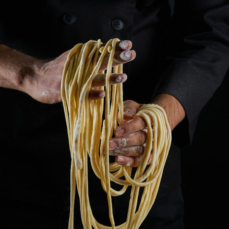 Person holding fresh noodles against a black background
