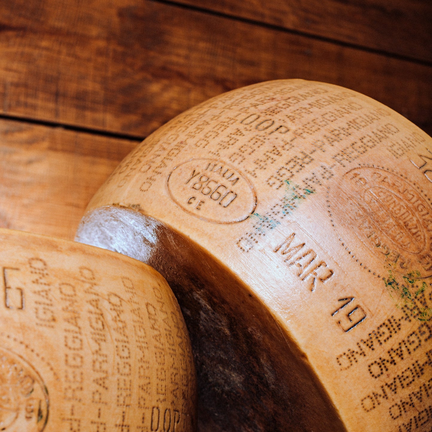 Two wheels of Parmigiano-Reggiano cheese on a wooden surface