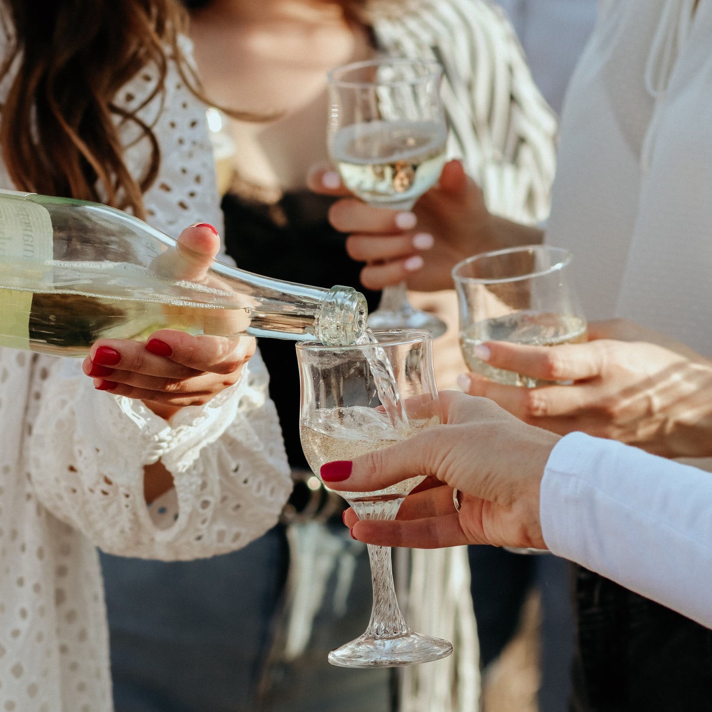 People pouring and holding glasses of white wine.