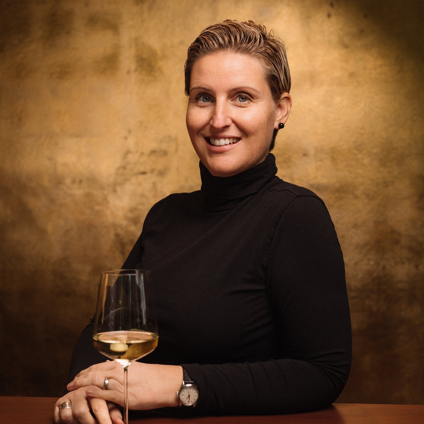 Person holding a glass of white wine against a warm brown background