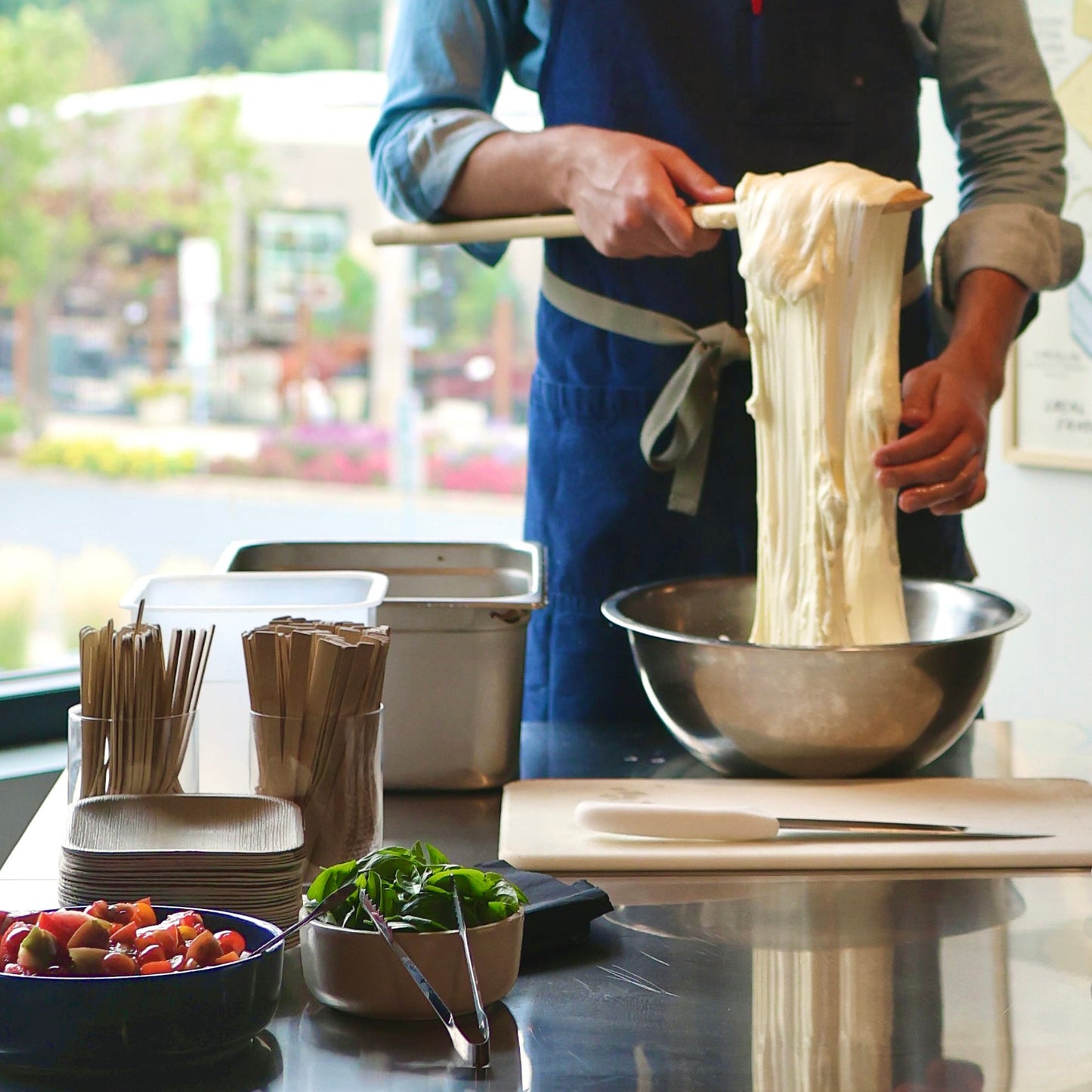 Person making mozzarella in a kitchen with various ingredients and utensils on the counter.
