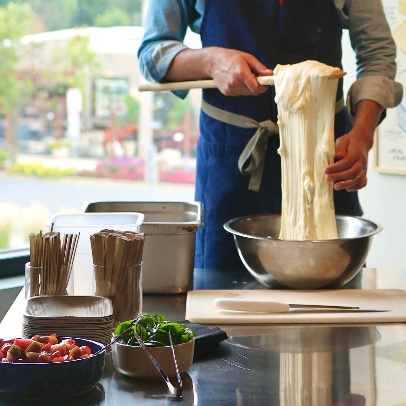 Person making mozzarella in a kitchen with various ingredients and utensils on the counter.
