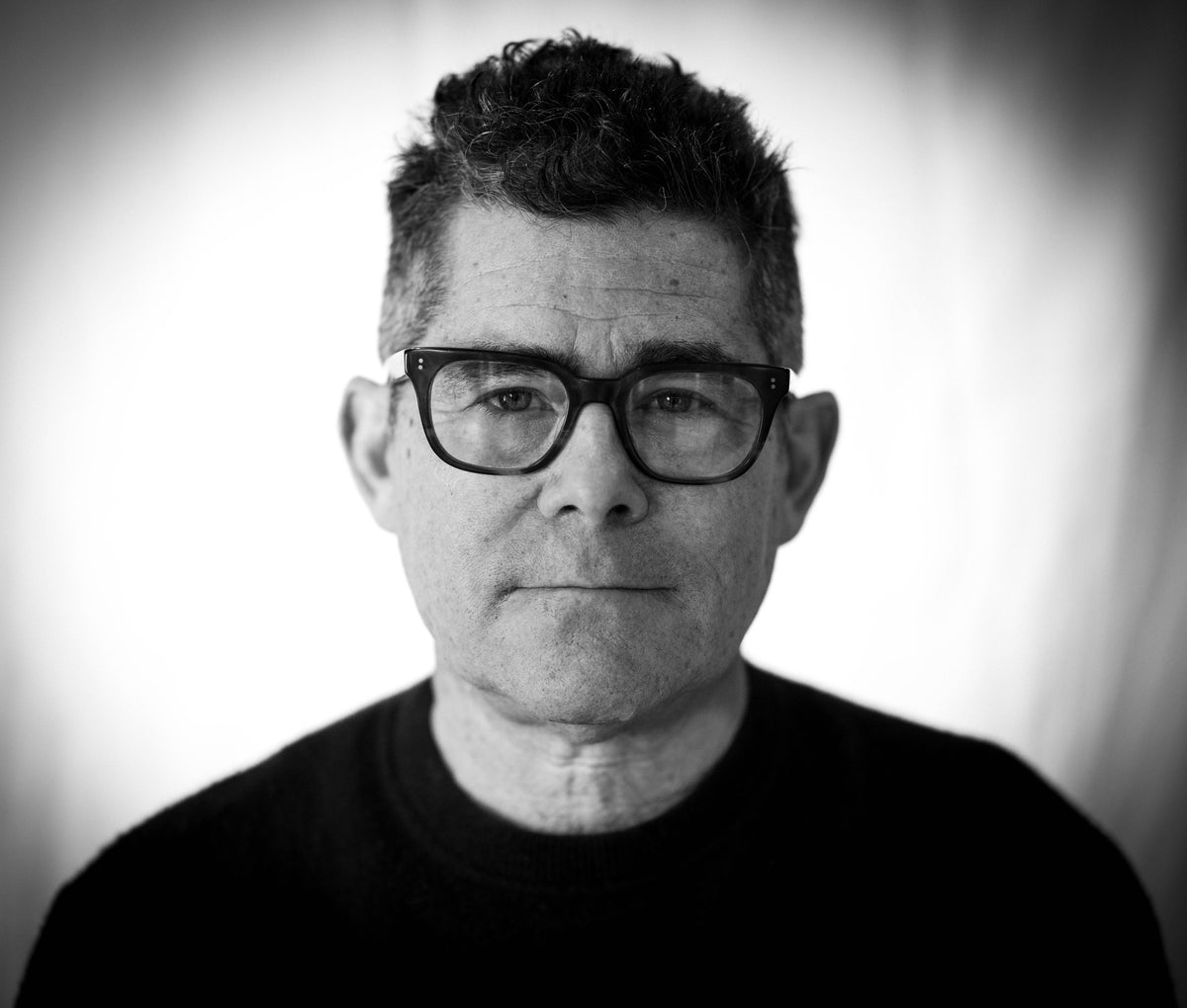 Black-and-white photo of filmmaker Jeffrey Reiner, a man with short hair and dark glasses, in a dark crewneck shirt
