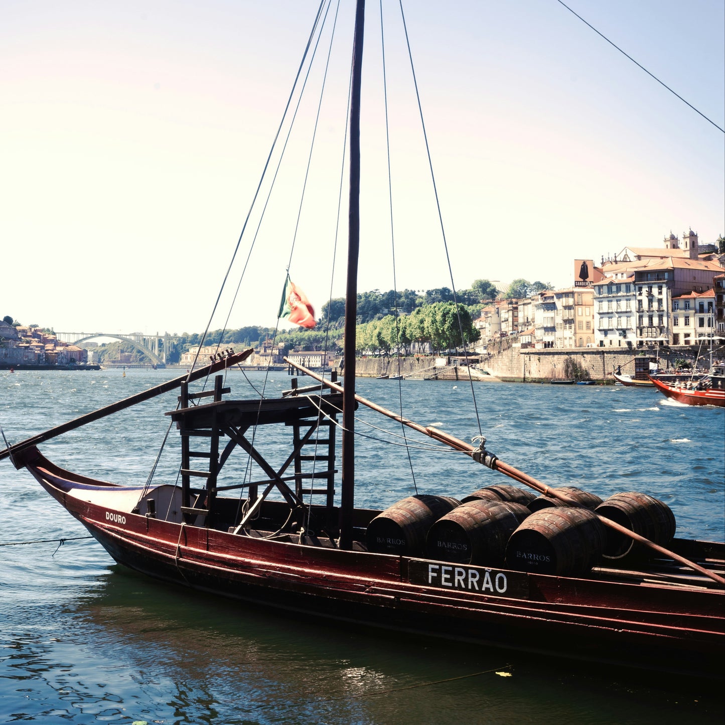 A traditional Portuguese ruyta boat with barrels on deck, labeled 'FERRAO', floating on the Douro River with Porto's cityscape in the background.
